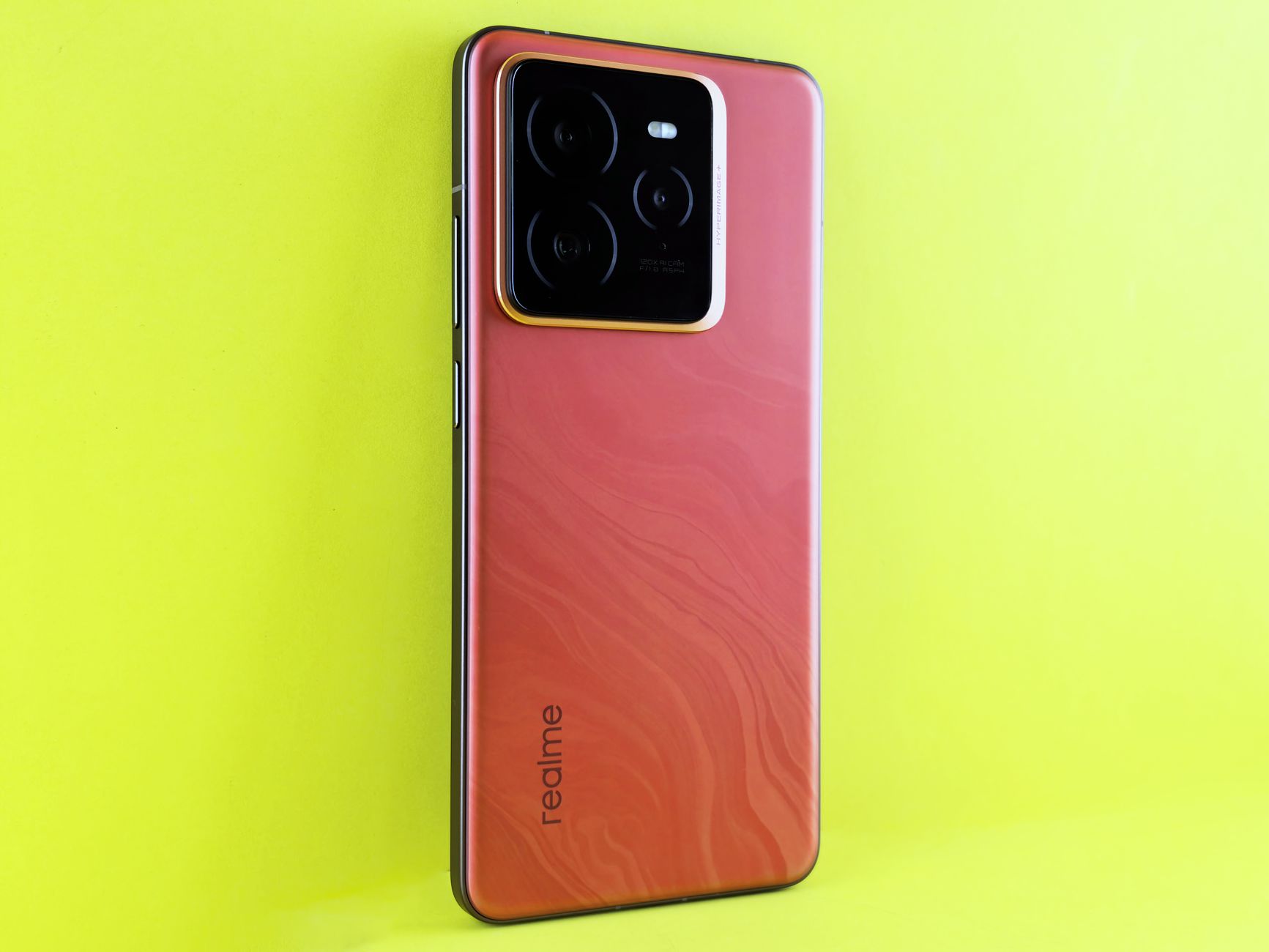 A sleek Realme smartphone with a red finish on a bright yellow background, showcasing the camera module.
