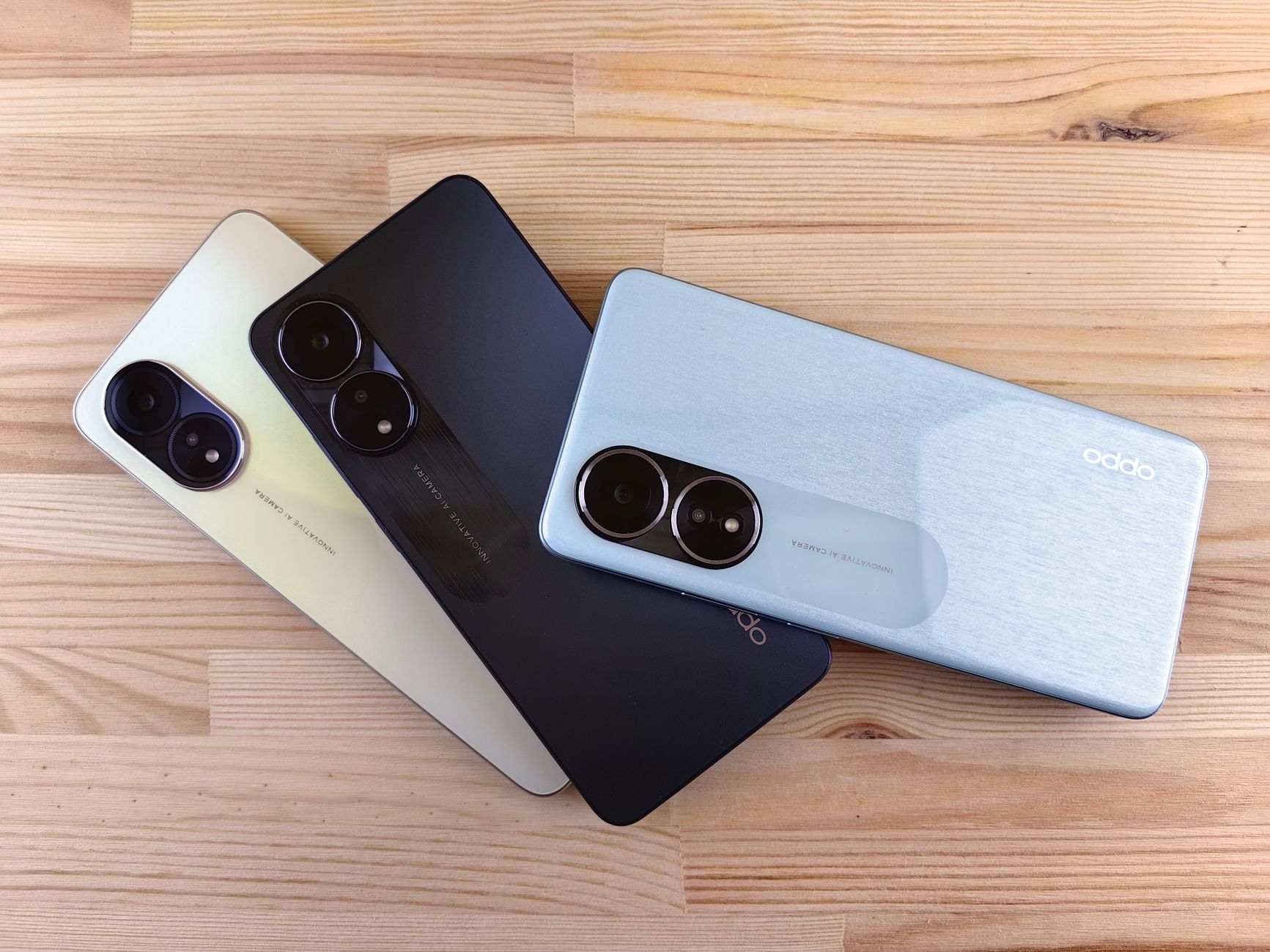 Three modern smartphones displayed on a wooden surface, showcasing design and color variants.