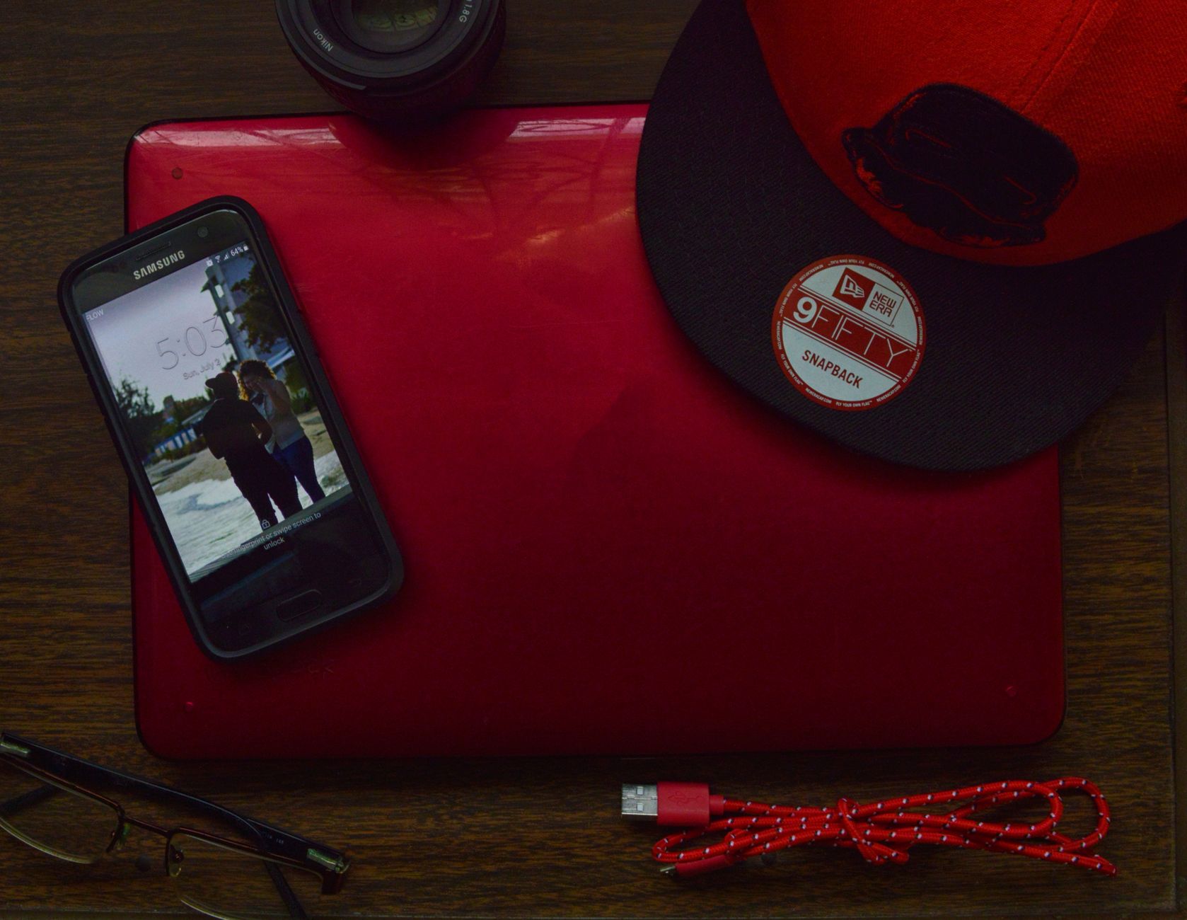 Stylish workspace with red laptop, cap, lens, and smartphone on a wooden desk.