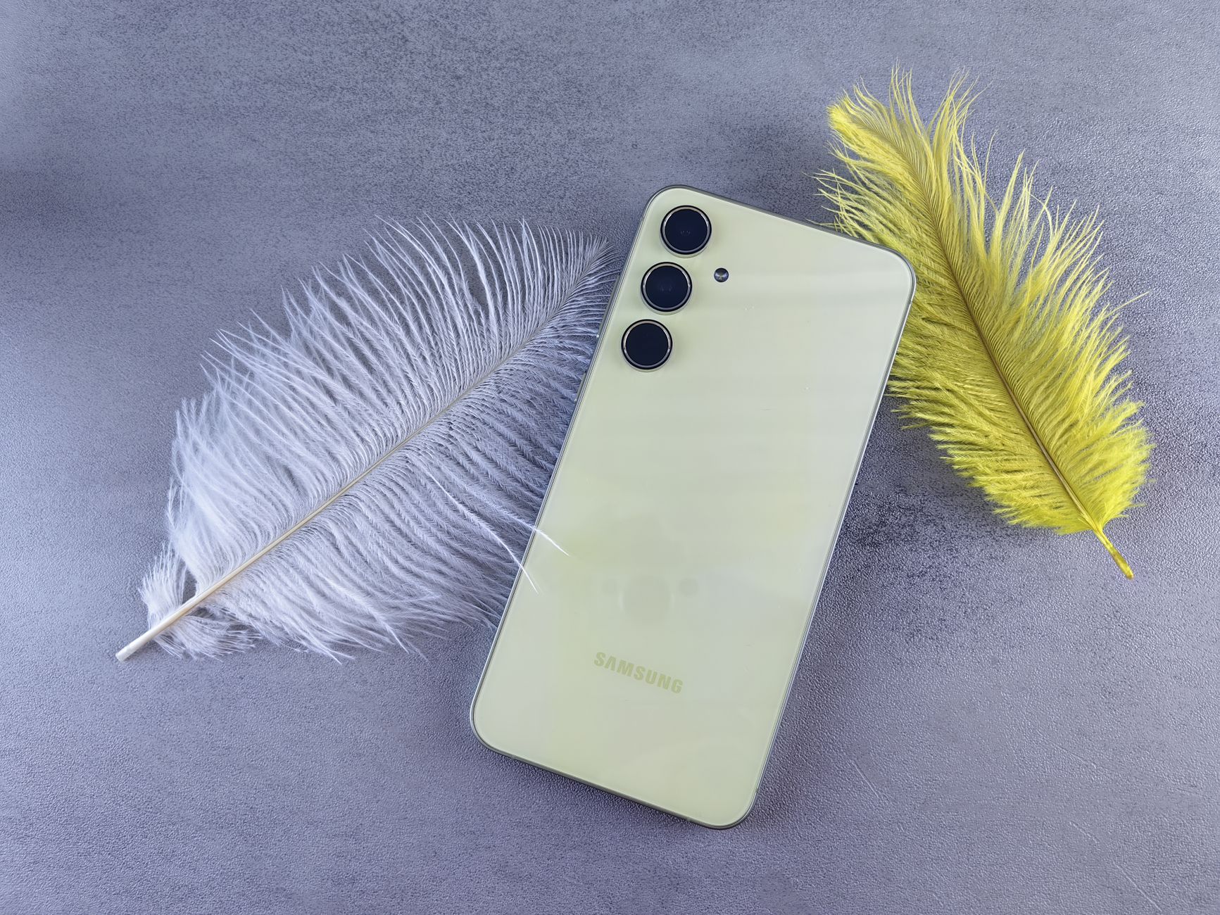Flat lay of a yellow smartphone with feathers against a gray background, perfect for tech and lifestyle themes.