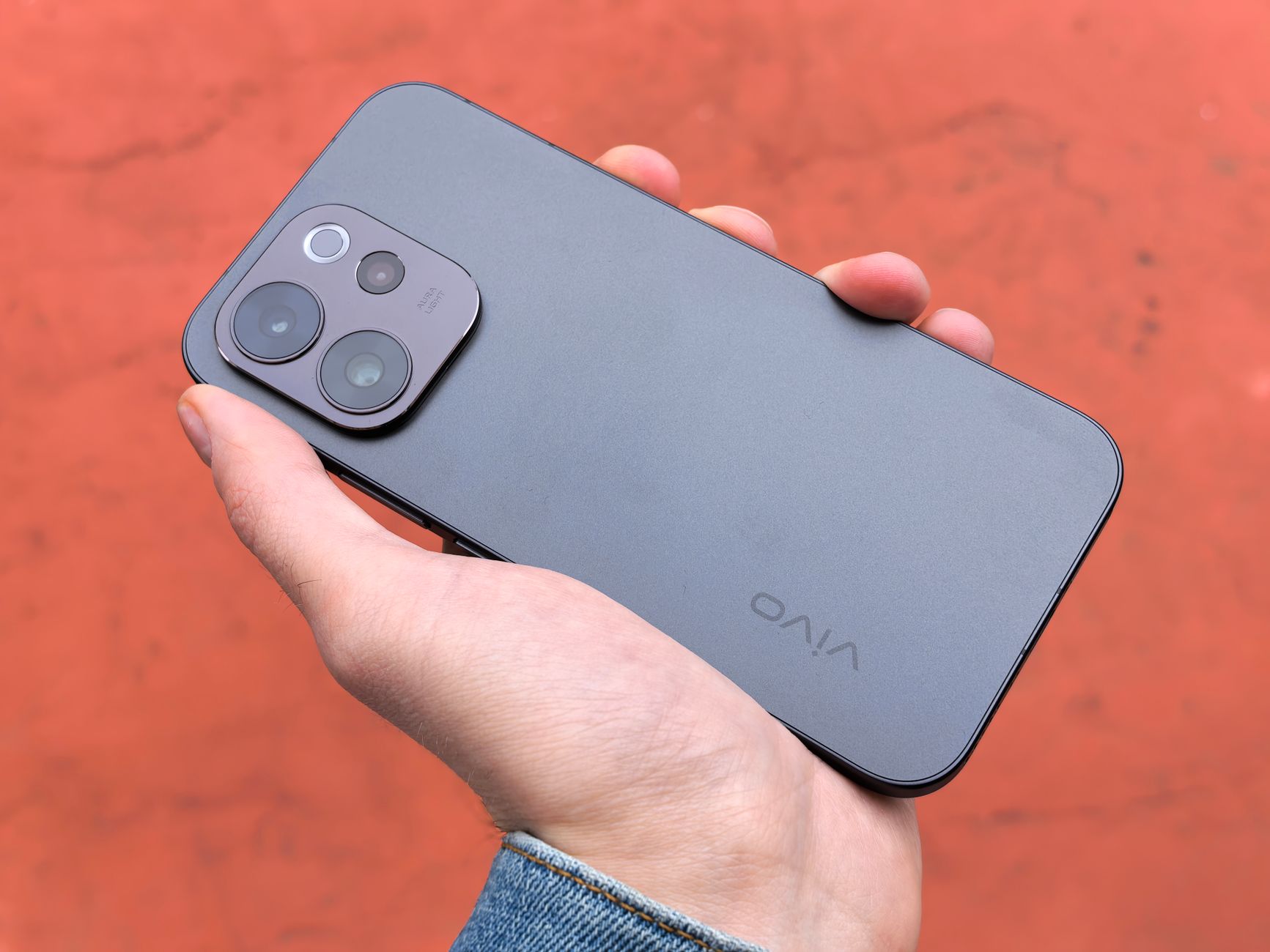A close-up view of a hand holding a sleek smartphone, captured outdoors against a warm backdrop.
