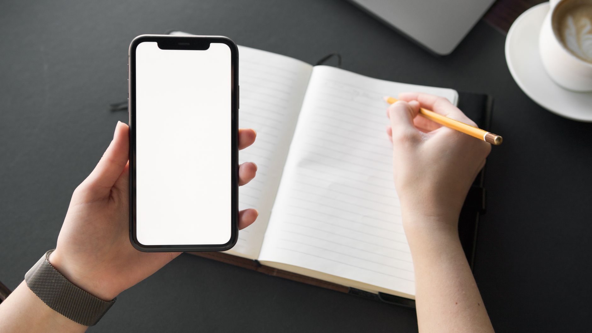 Blank smartphone screen in hand next to open notepad with pencil writing.