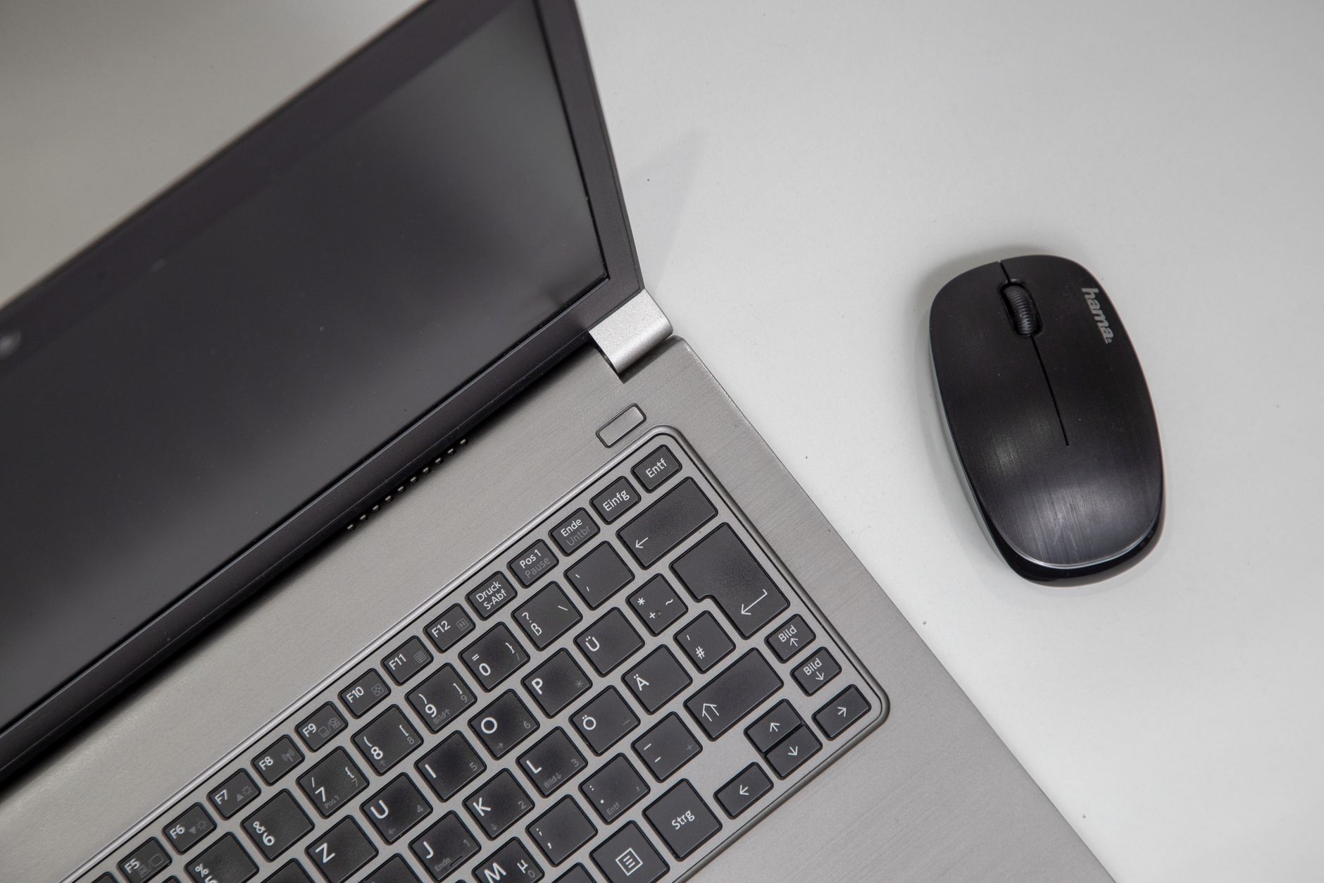 Overhead view of a laptop with a wireless mouse on a white table.