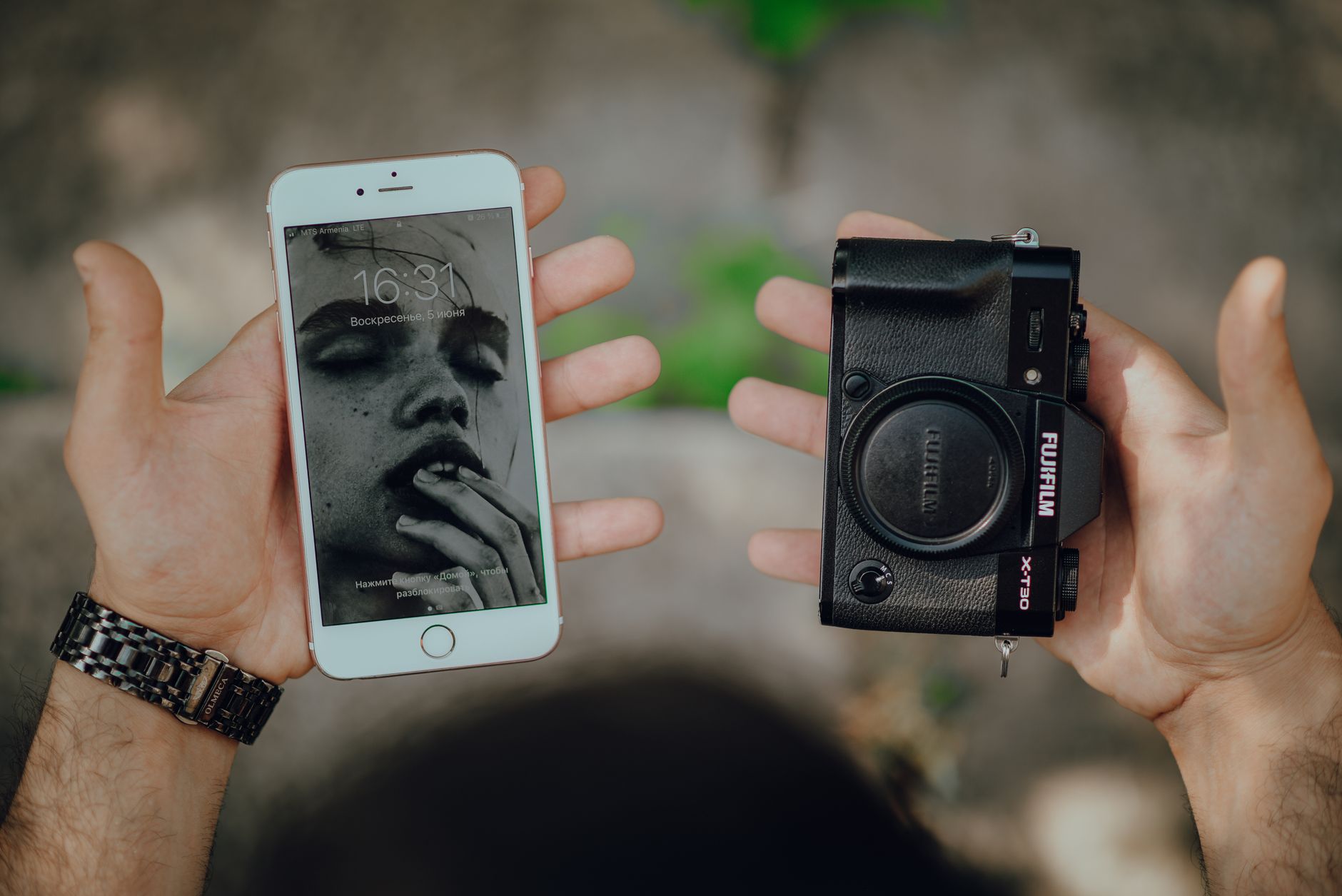Hands holding a smartphone with art wallpaper and a camera body outdoors.