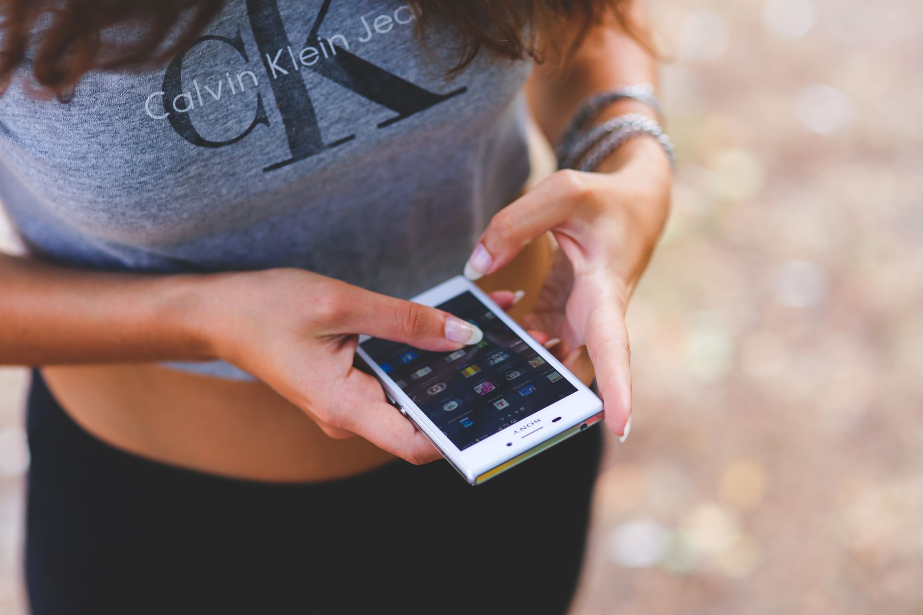 Young woman interacting with smartphone outdoors, wearing casual crop top.