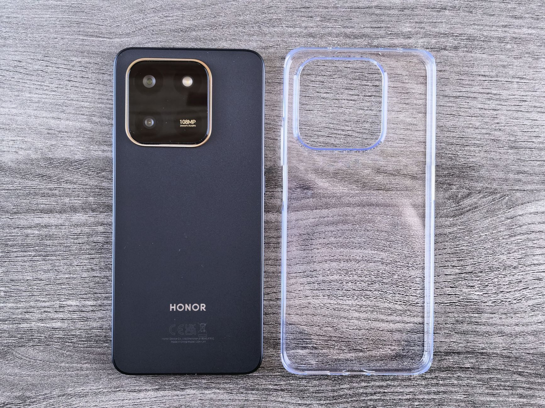 A sleek black smartphone paired with a transparent phone case on a wooden surface.