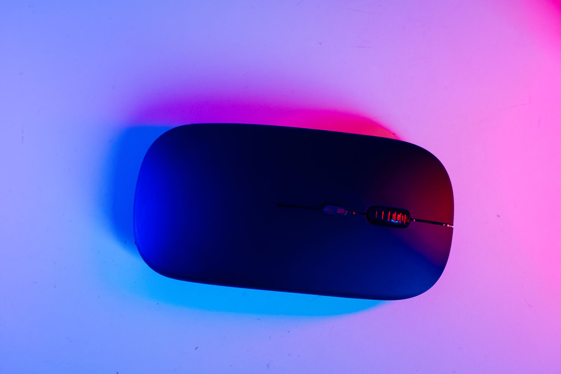 Sleek black wireless computer mouse under vibrant blue and pink lighting for a tech-focused aesthetic.