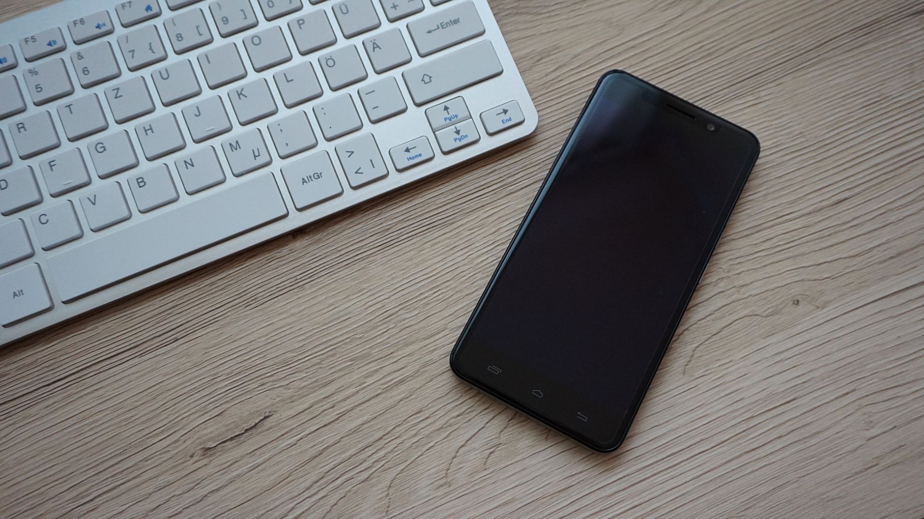 A close-up image of a keyboard and smartphone on a wooden desk, showcasing modern technology essentials.