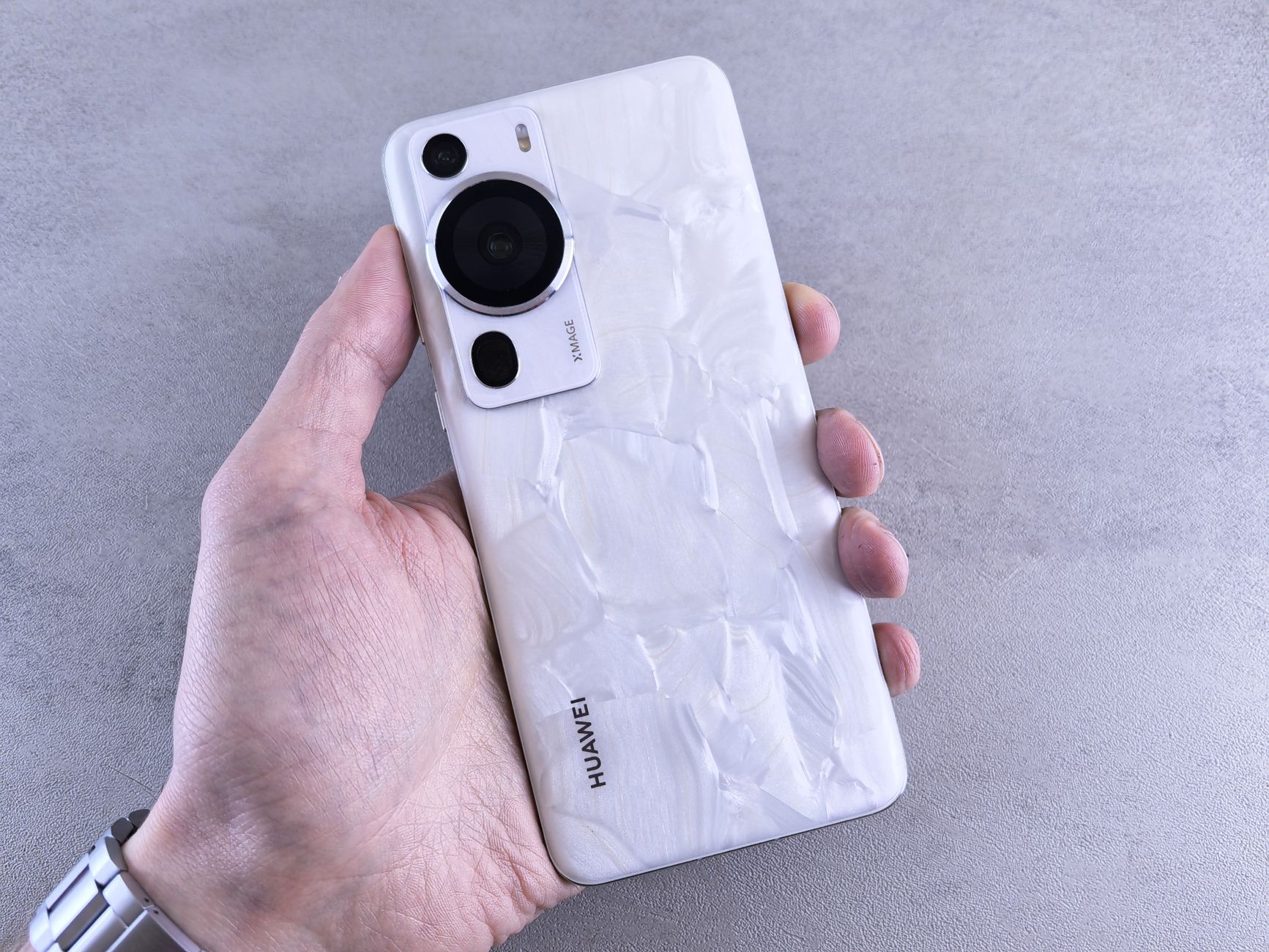 A close-up view of a hand holding a Huawei smartphone with a textured back panel in a studio setting.