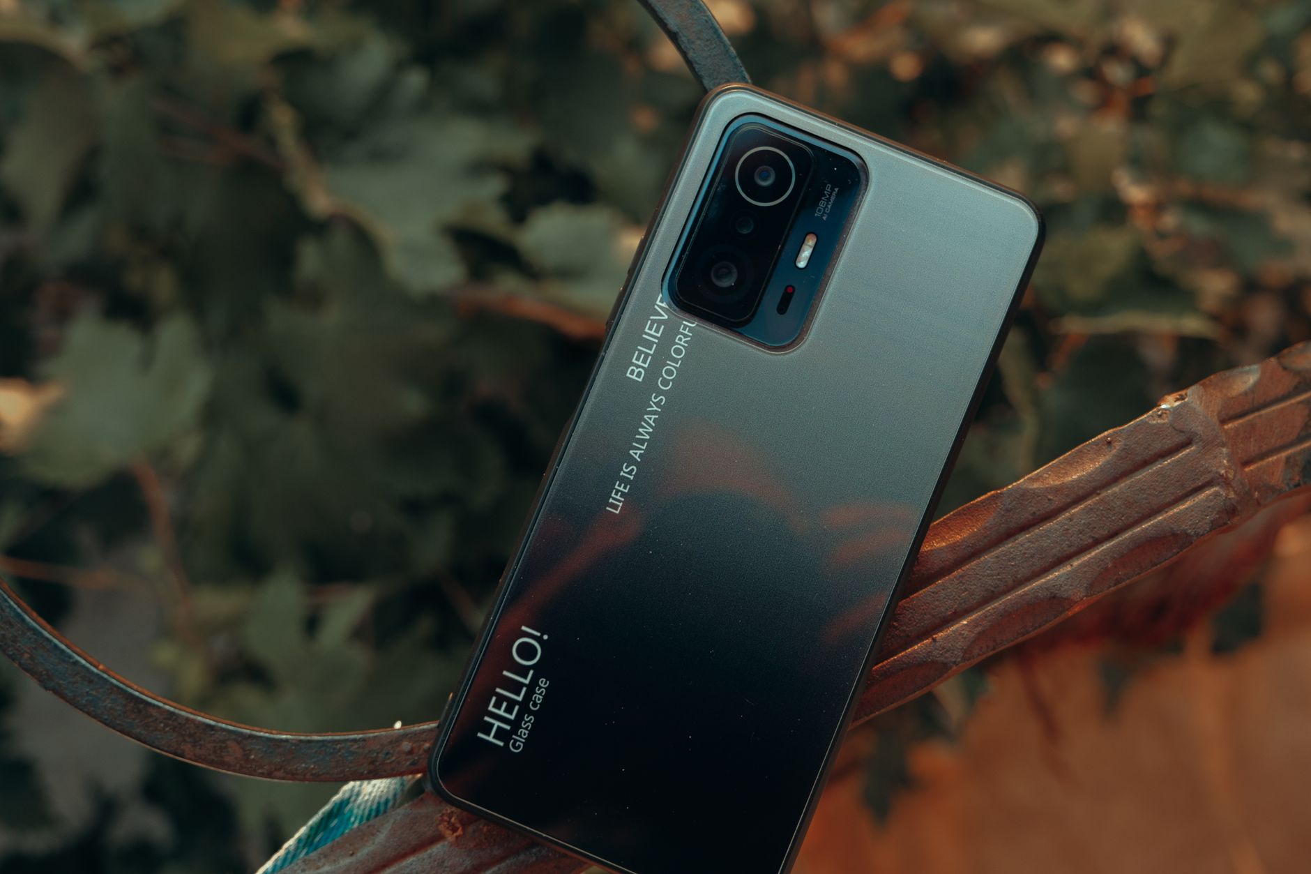 A close-up of a smartphone placed outdoors with a nature background, showcasing design details.