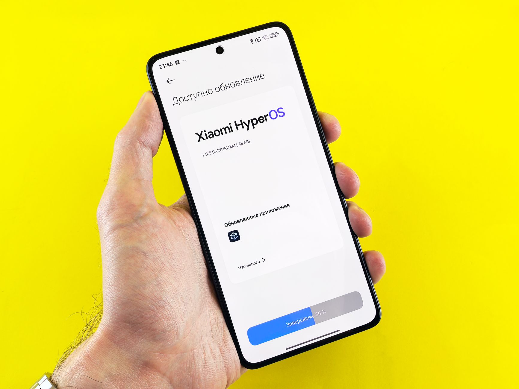 Hand holding smartphone showing Xiaomi HyperOS update screen on yellow background.