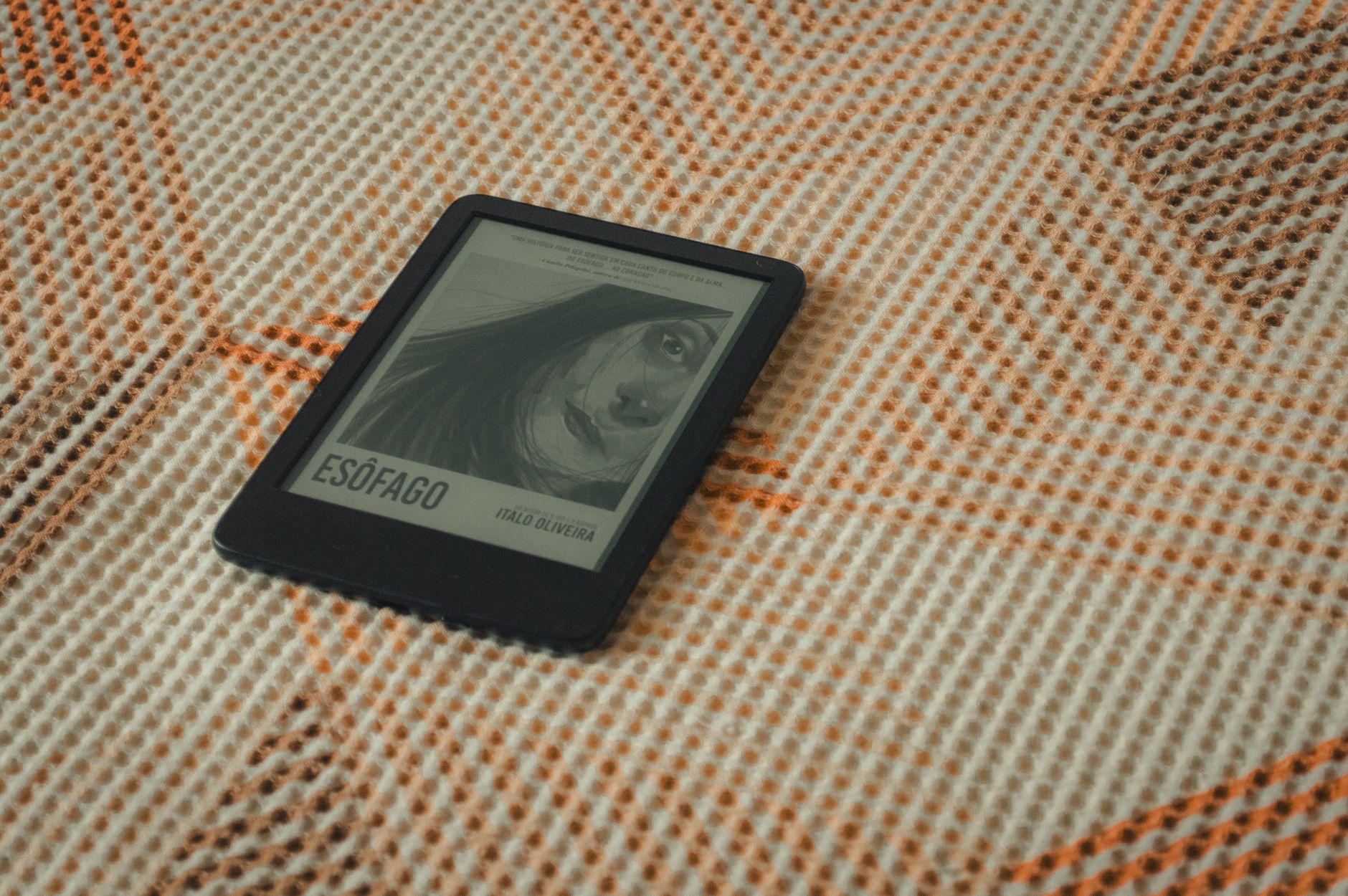 An e-reader displaying a book cover placed on a patterned fabric with warm tones.