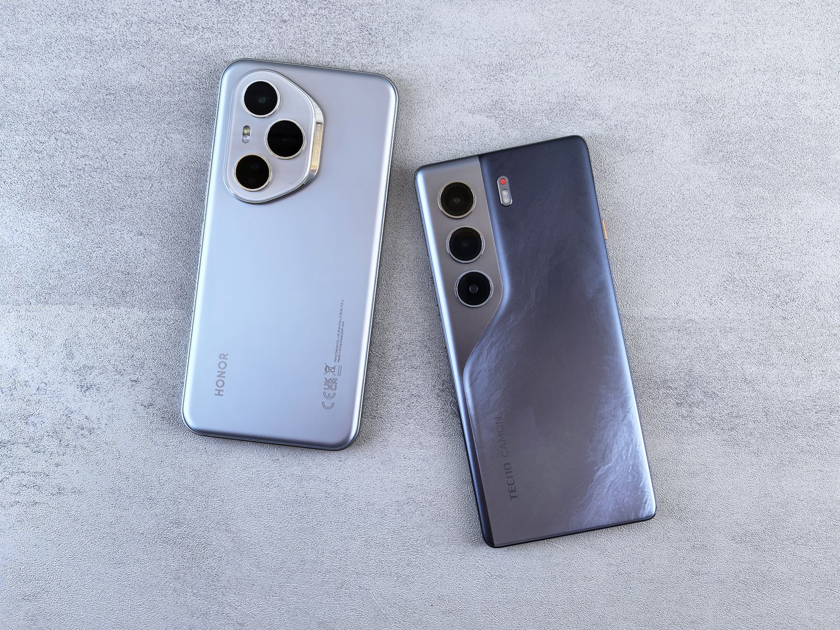 Two modern smartphones displayed on a concrete surface, showcasing different camera designs and styles.