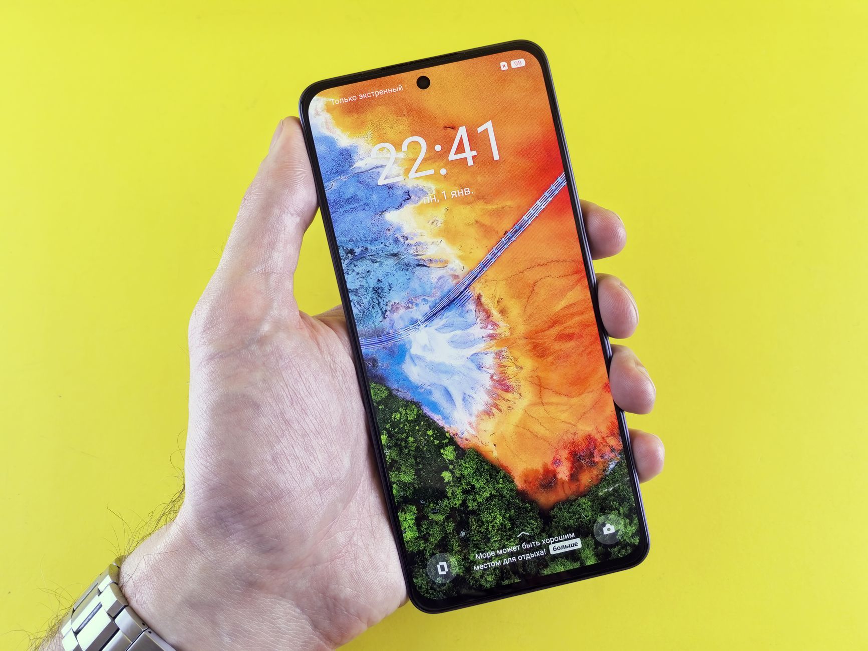 Close-up of a hand holding a smartphone with vivid colors on its screen, set against a yellow background.