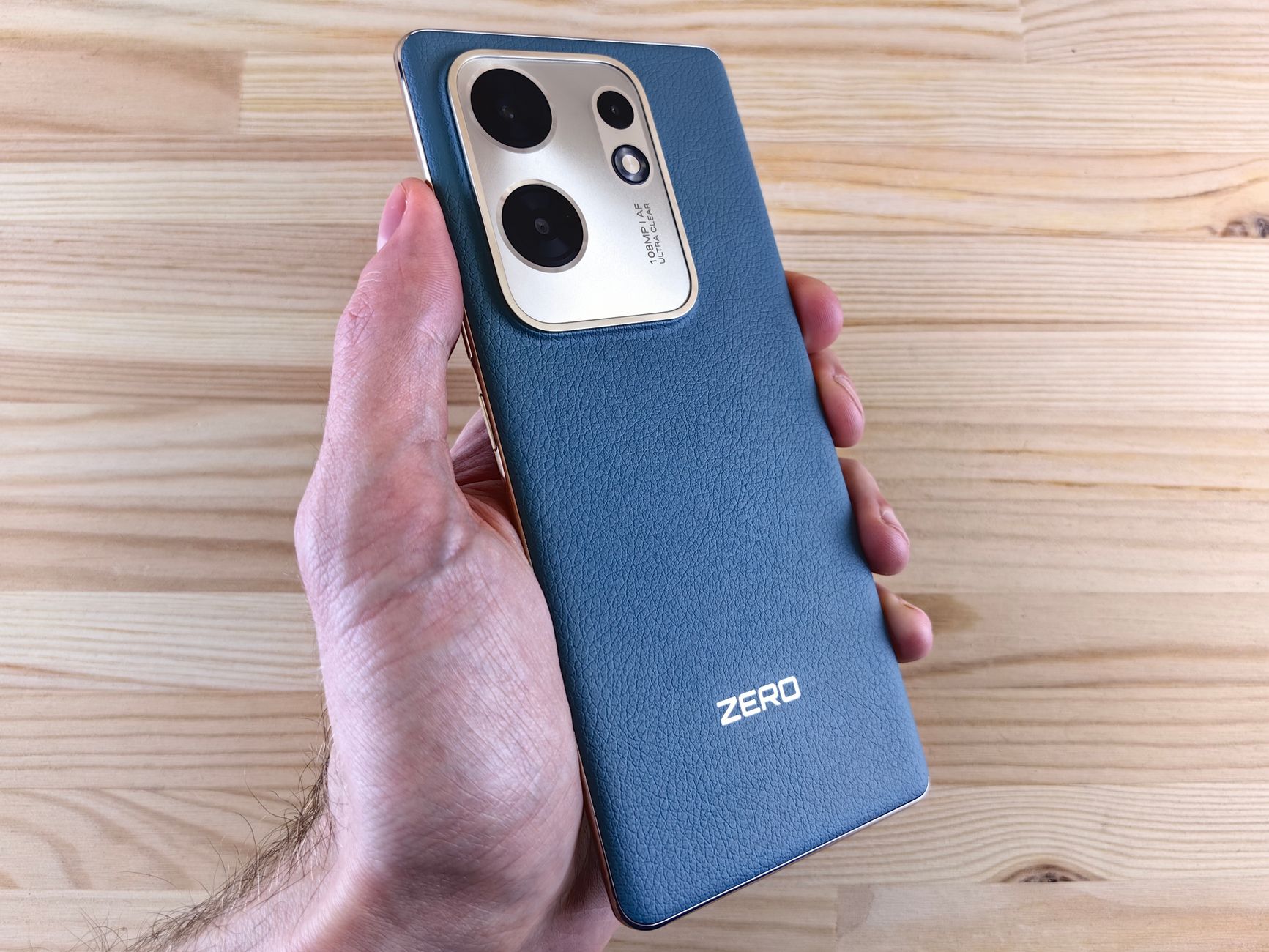Hand holding a sleek smartphone with dual camera design on a wooden surface.