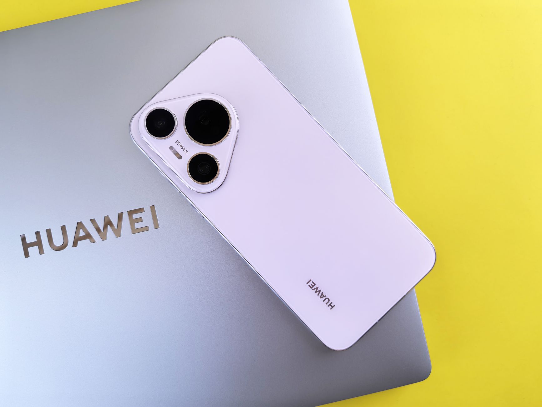 A sleek smartphone with a triple camera setup rests on a laptop, contrasting against a vibrant yellow background.