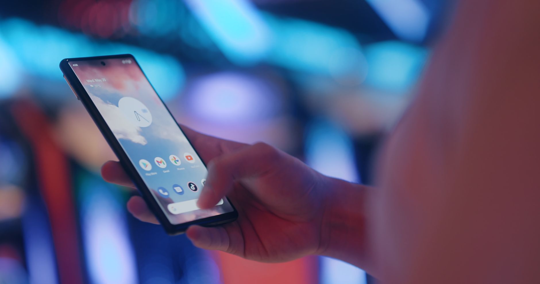 A hand holds a smartphone displaying apps, highlighted by vibrant neon lights.