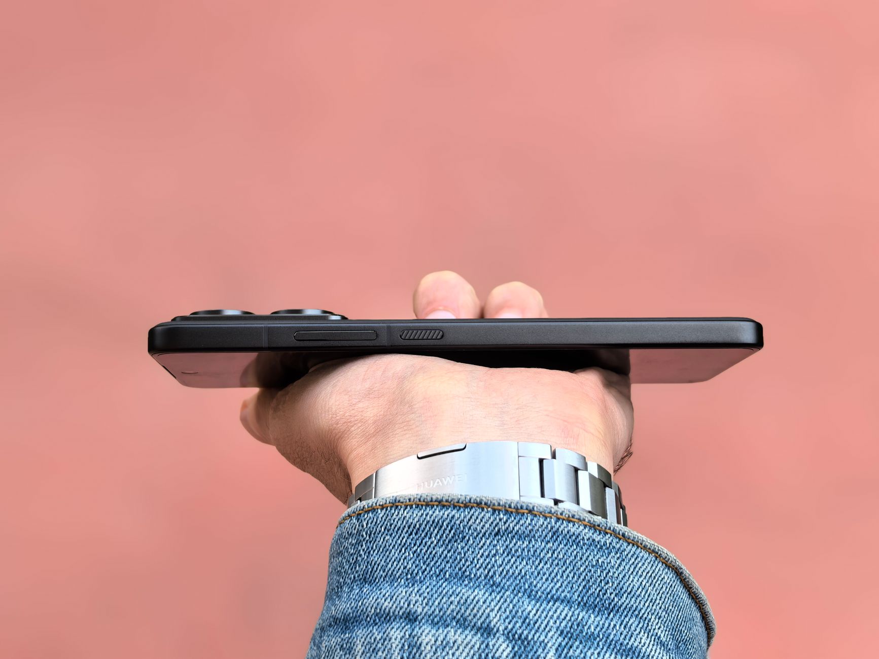 A person holding a smartphone horizontally against a soft pink backdrop, showcasing the device's slim profile.