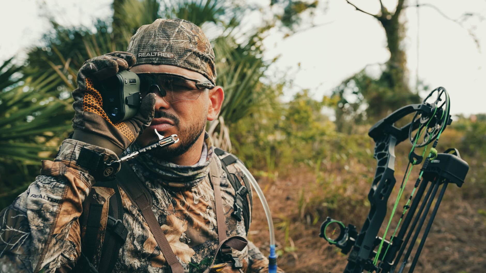 Hunter in camouflage gear using a rangefinder while outdoors, showcasing focus and precision.