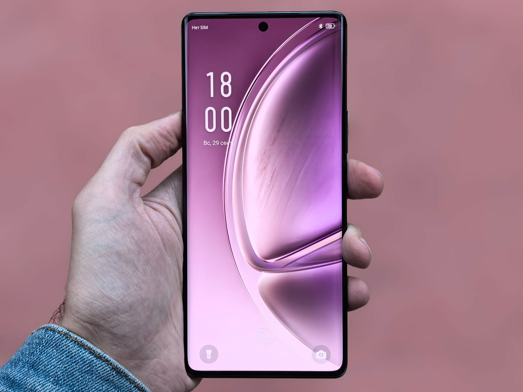 A person holding a sleek, modern smartphone with a purple screen against a plain background.