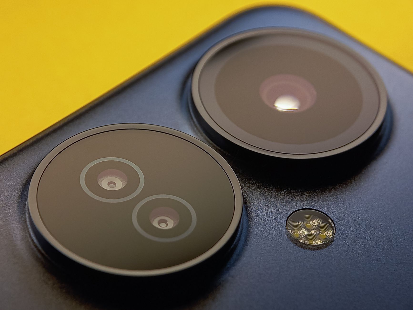 Extreme close-up of smartphone camera lenses with vibrant yellow background, showcasing modern technology.