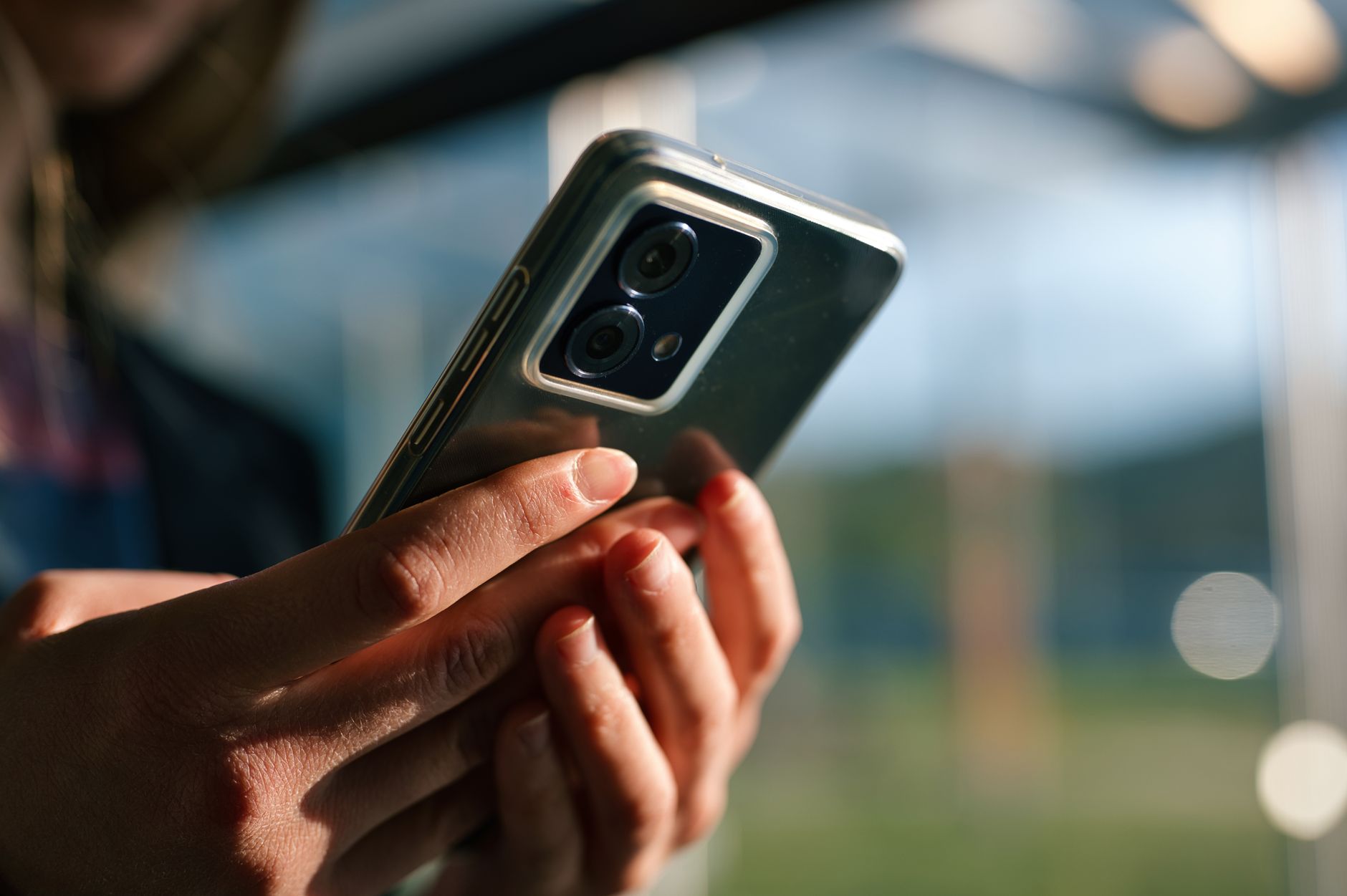 Focused view of hands holding a modern smartphone outdoors with blurred background.