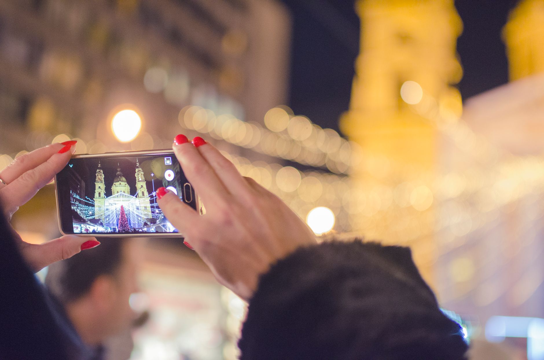 Woman taking a night photo of a cityscape with a smartphone, showcasing bright lights and towers.
