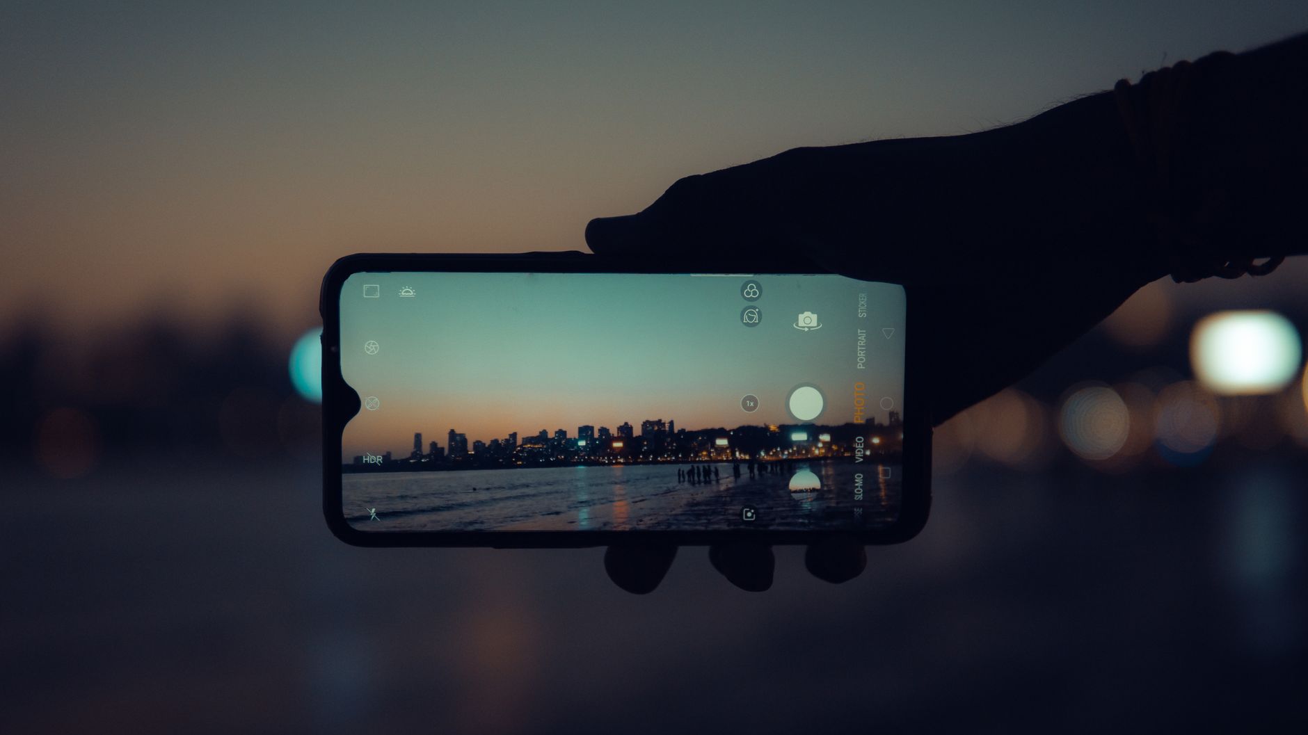 A smartphone capturing the Mumbai skyline at sunset with a clear reflection on its screen.