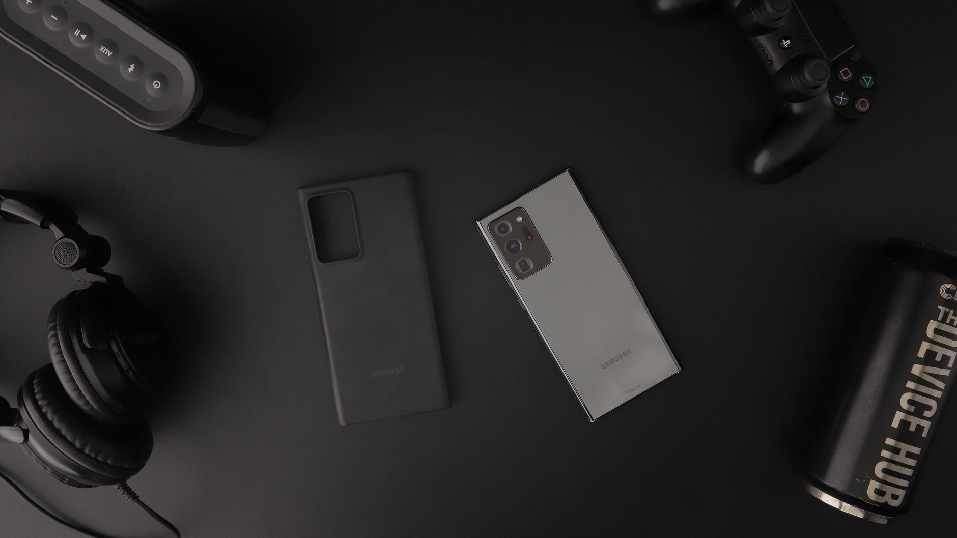 Flat lay of modern electronic gadgets including headphones, phone, and gaming controller on a table.