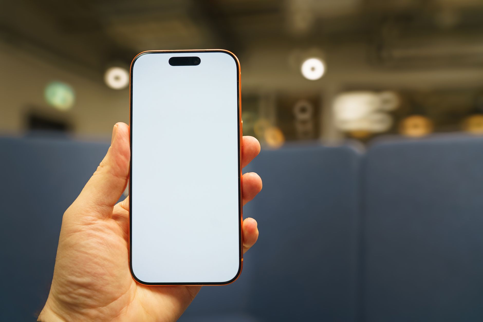 Close-up of a hand holding a smartphone with a blank screen indoors, suitable for app or tech mockups.