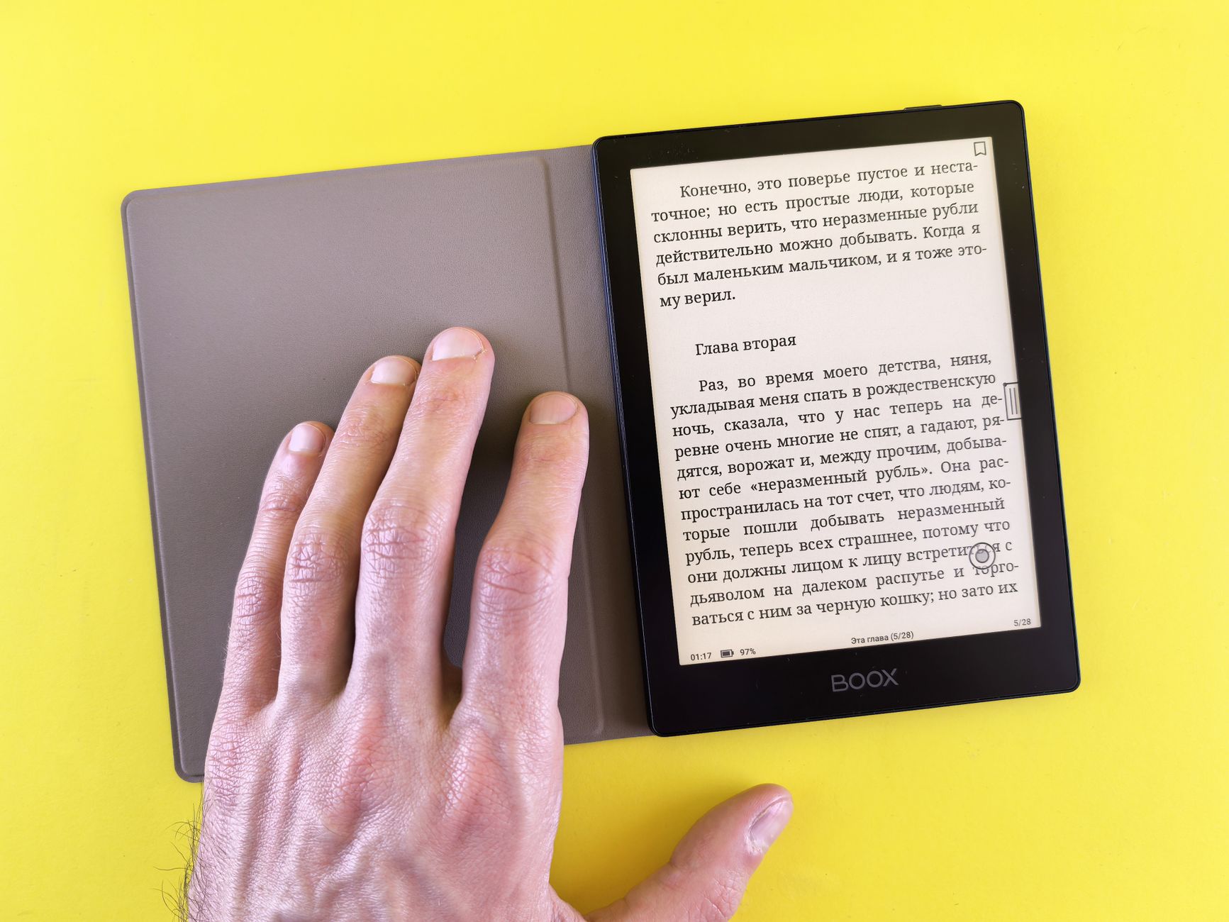 A hand holding an e-reader displaying text on a bright yellow background, showcasing modern digital reading.