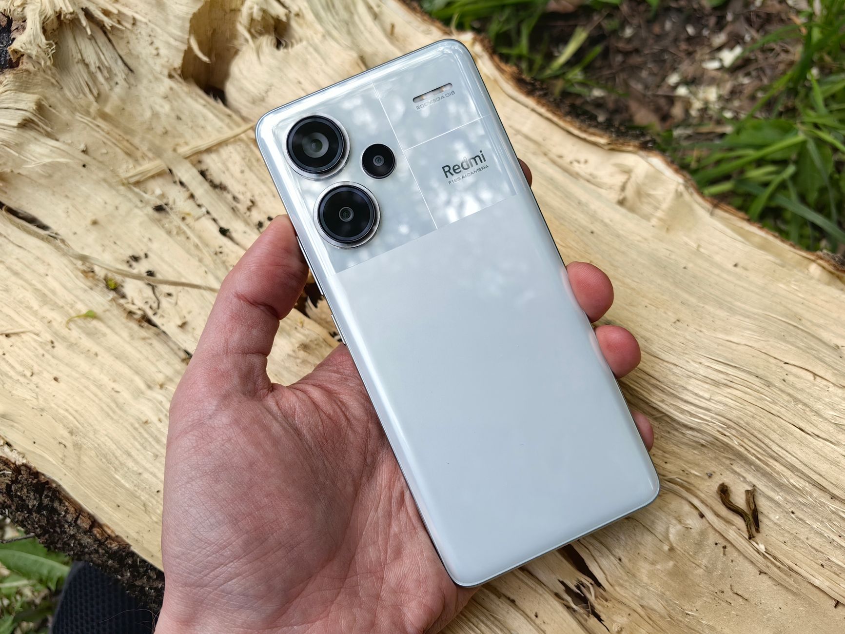 Close-up of a hand holding a modern white smartphone with dual lenses outdoors.